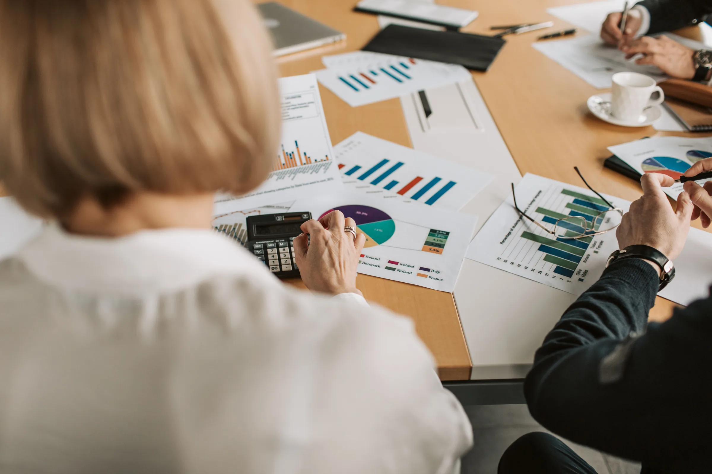 Colleagues reviewing printed financial charts with a calculator at a meeting table