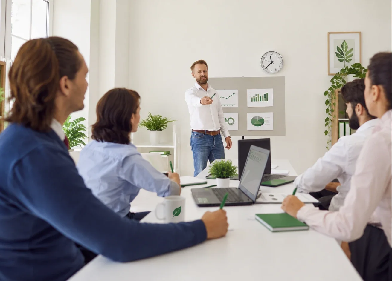 A colleague presenting green sales charts to a team around a meeting table