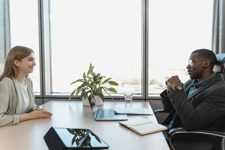 Two colleagues talking across a meeting-room table by a window