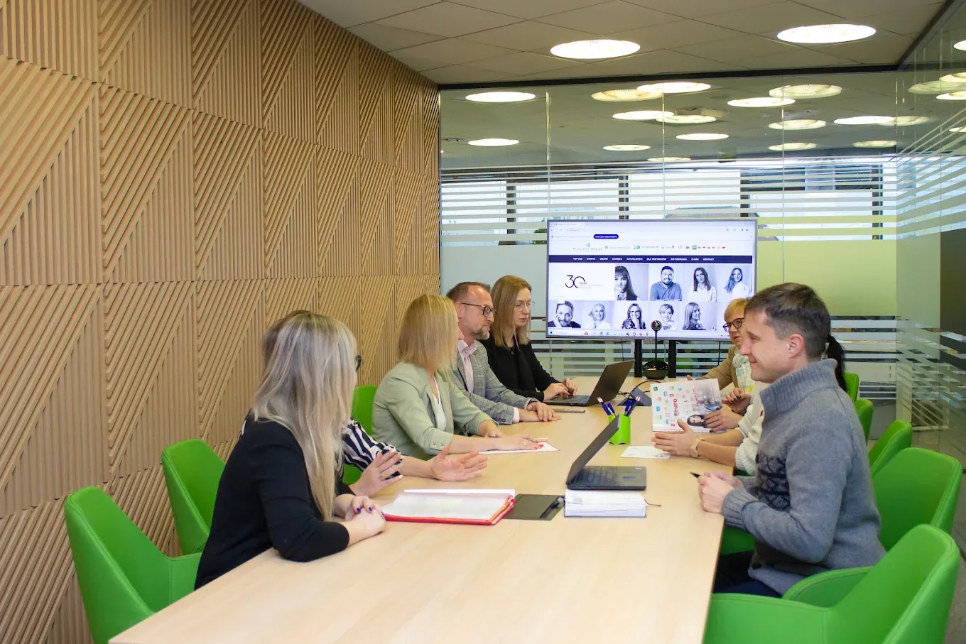 BDG colleagues planning around a meeting-room table, a marketplace listing page on the screen behind them