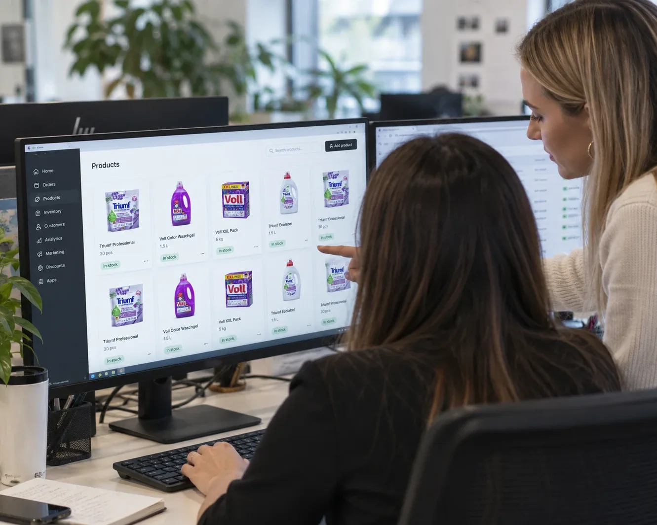 Two colleagues at a monitor reviewing Triumf and Voll listings in an online store’s product dashboard
